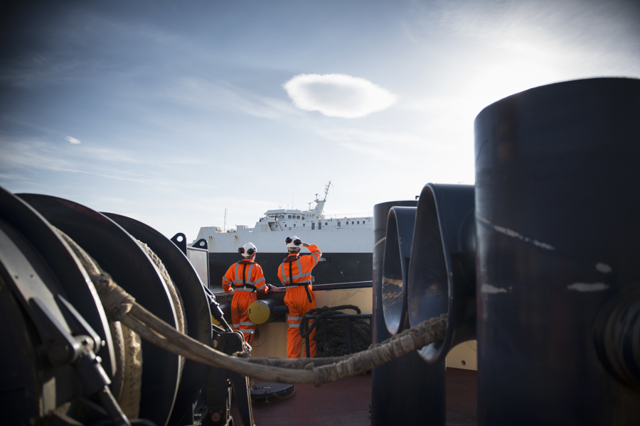 Two workers on a ship look towards another ship.