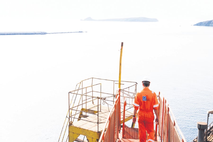 Seafarers at work on scaffolding, ocean and mountains in the background.