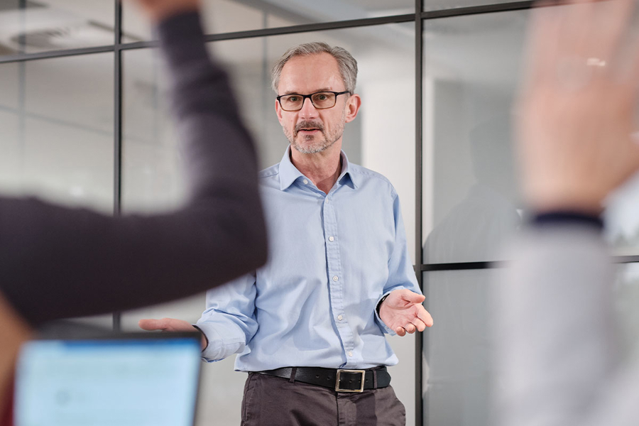 A trainer standing at the front of a room, framed between blurred hands to show they are answering questions.