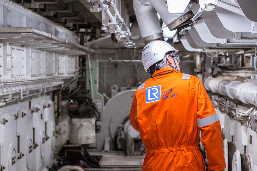 Worker in orange boiler suit surveys ship.