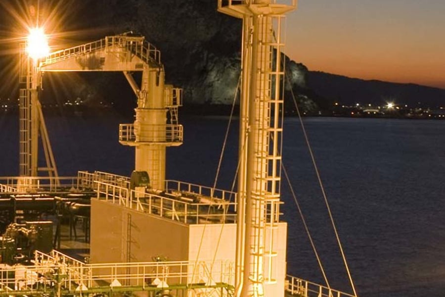 Ship lit up by lights at night, mountains in the background.