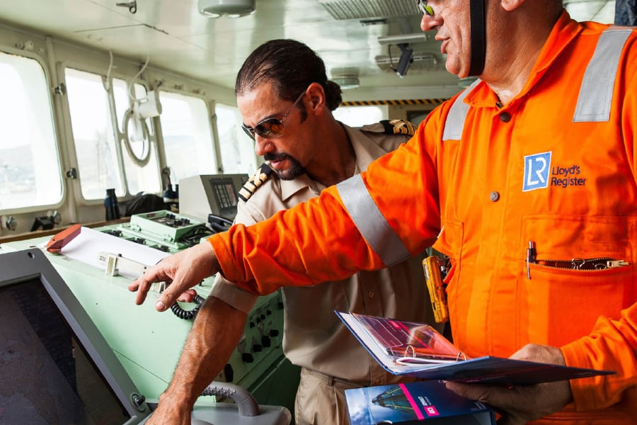 Two seafarers stand at a ships navigation desk